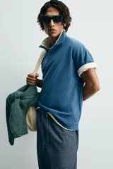 Polo de algodón con estructura piqué, color azul deslavado. Presenta un corte regular fit, cuello solapa con cierre de botones, manga corta con acabado en rib y bajo asimétrico con aberturas laterales.