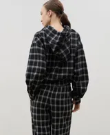Camisa de manga larga con capucha, confeccionada en tejido liviano con estampado a cuadros. Presenta cierre frontal con botones y lazo regulable en la cintura.