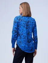 Camisa de gasa estampada con flores negras sobre fondo azul. Cuello con solapa y abertura central con botones.
