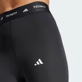 Calza capri deportiva Adidas Techfit de color negro, con diseño de compresión y tiro alto. Presenta una cintura elástica ancha con la inscripción "TECHFIT" repetida y el logo de la marca en blanco en la pierna izquierda.