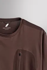 Camiseta de entrenamiento de manga larga Zara Athleticz de color marrón, corte regular fit y cuello redondo. Está confeccionada en tejido técnico elástico de secado rápido y cuenta con un bolsillo en el pecho con cierre de cremallera.