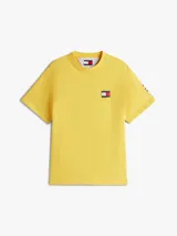 Remera amarilla de algodón con corte amplio, cuello redondo y hombros caídos. Presenta un logo pequeño de Tommy Hilfiger en el pecho, un logo en la manga y un logo grande en la espalda. Pertenece a la colección Hilfiger Sailing.