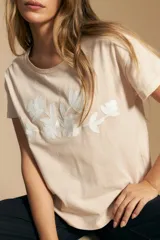 Remera de manga corta color negro con cuello redondo y un aplique bordado de flores y hojas en color beige claro en el centro del pecho.