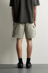 Bermuda cargo color negro de corte relaxed fit, confeccionada en tejido de algodón con elasticidad y efecto lavado. Cuenta con cintura elástica ajustable con cordón, bolsillos frontales y bolsillos laterales tipo cargo con solapa en las perneras.