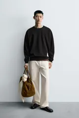 Sudadera negra de corte relaxed fit, confeccionada en tejido técnico interlock de algodón con elasticidad. Presenta cuello redondo, manga larga y una etiqueta aplicada en el bajo. Los acabados son en rib.