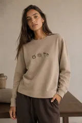 Sweater de calce relajado en color beige con cuello redondo y mangas largas. Presenta un bordado frontal exclusivo con motivos de un mate, un sol y un caballo.