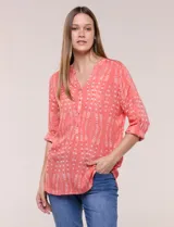 Blusa turquesa de silueta suelta confeccionada en tejido liviano, con escote en V, pequeña cartera frontal con botones decorativos y mangas 3/4 con presilla para arremangar. Presenta patrón estampado geométrico tipo tie-dye y ruedo curvo.