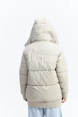 Campera puffer larga con capucha, color beige, de ajuste relajado. Presenta cierre frontal con botones a presión, bolsillos laterales con cierre y puños tejidos acanalados.