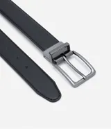 Cinturon reversible negro para hombre, de cuero sintetico con textura y hebilla metalica cuadrada de color plateado oscuro.