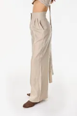 Pantalón de lino blanco de corte ancho y fluido, con cintura alta que incorpora una sobrepretina ancha desmontable con pliegues horizontales.