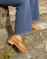 Zapato acordonado estilo oxford de cuero vacuno en color plateado metalizado, con diseño brogue, suela de goma y taco de madera.