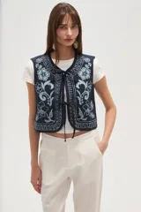 Chaleco sin mangas, color azul marino, con bordados florales en tono celeste claro. Presenta un escote en V y se cierra al frente con lazos ajustables.