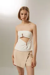 Top strapless color blanco, con diseño cut-out frontal y detalle de aros metálicos en el centro. Presenta un ajuste al cuerpo y cierre posterior.