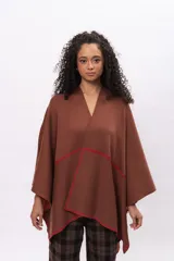 Ruana de algodón en color marrón con detalles de costura a mano en contraste color rojo en los bordes. Diseño envolvente de corte asimétrico y mangas amplias.