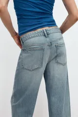 Jeans de denim de tiro medio y corte relaxed con diseño de cinco bolsillos, trabillas en la cintura y cierre frontal con cremallera y botón metálico.