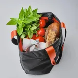 Bolso tote negro de tela resistente al agua, con asas de correa negras con borde naranja. Tiene cierre principal, bolsillos laterales (uno con cierre), seis bolsillos internos, diseño plegable y capacidad de 14,5 litros.