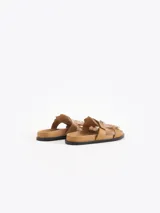 Sandalias planas color tostado de cuero vacuno, con capellada adornada con flecos y una tira con hebilla metálica.