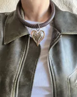 Gargantilla marrón con dije plateado en forma de corazón con borde dorado.