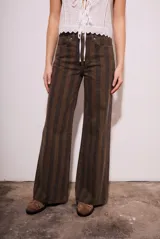 Pantalón de jean de tiro medio, corte wide leg acampanado, con estampado de rayas verticales en tonos marrón oscuro y negro.