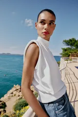 Top de punto color marrón oscuro, con cuello subido, manga sisa con hombreras, pliegues y espalda descubierta con cierre trasero de botones.