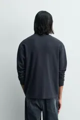 Camiseta de manga larga para hombre con corte relajado, confeccionada en tejido con estructura waffle. Presenta un cuello redondo tipo panadero con cierre frontal de botones a presión.