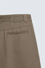 Pantalón de corte baggy fit confeccionado en tejido de algodón con estructura diagonal y efecto lavado. Presenta cintura con pliegues frontales, bolsillos laterales, bolsillos traseros de vivo y un bolsillo lateral adicional con doble vivo en la pernera. Cierre frontal con cremallera y botón.