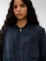 Campera tipo bomber color azul, con cierre frontal, cuello redondo acanalado, bolsillos frontales con solapa y cintura y puños elásticos.