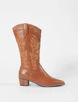 Botas texanas de caña media en color marrón, confeccionadas en cuero vegano. Presentan bordados decorativos en contraste a lo largo de la caña y en la puntera, con un taco cuadrado de madera y punta fina.