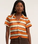 Blusa de punto con diseño de rayas en zigzag de colores naranja, marrón, verde menta y blanco. Presenta cuello polo, escote en V y mangas cortas, con un corte boxy holgado.