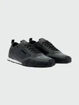 Zapatillas deportivas Diesel modelo S-Pagodha, con diseño de paneles en cuero y gamuza en tonos verde oscuro y negro. Presentan suela de goma robusta con relieve geométrico que se extiende hacia la puntera, cordones negros y detalle de logo en la lengüeta.