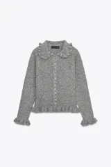 Chaqueta de punto gris con cuello solapa, manga larga y cierre frontal con botones. Presenta detalles de volantes en el cuello, los puños y el ruedo.