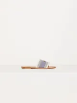 Sandalia chata confeccionada en denim, con flecos en la capellada y aplique metálico.