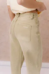 Jean de calce relajado y pierna amplia color beige, con tiro alto y detalle de recortes y costuras visibles.