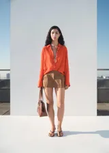 Camisa de corte oversize color naranja, con cuello camisero, cierre frontal de botones y mangas largas con puños abotonados. Presenta un acabado con efecto arrugado.