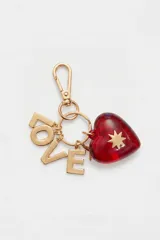 Llavero metálico dorado con gancho mosquetón y argollas, decorado con dijes en forma de letras que forman la palabra "LOVE" y un dije de corazón rojo de acrílico traslúcido con una estrella dorada en relieve.
