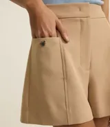 Short sastre de cintura alta con estructura definida, bolsillos laterales decorados con tachuelas metalizadas y recortes delanteros con costura aparente.