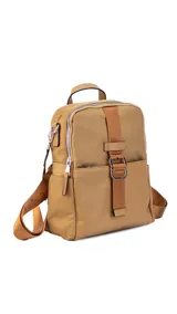 Mochila de tamaño mediano, color beige claro, con cuerpo principal de tela impermeable y detalles en simil cuero liso en la parte inferior y correas. Presenta un asa superior corta y correas ajustables para llevar al hombro o cruzada. Cuenta con un bolsillo frontal con cierre y un detalle decorativo de correa con hebilla metálica rectangular.