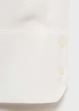 Camisa blanca de tejido fluido con cuello camisero, manga larga con puños abotonados y cierre frontal de botones ocultos.