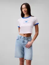 Remera cropped de manga corta color rosa pálido, con cuello redondo y ribetes azules. Estampado frontal con el logo de Calvin Klein y la inscripción 'New York City' en azul.