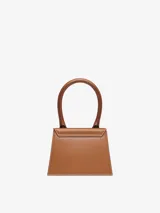 Bolso mini de cuero color marrón, con asa corta reforzada y correa larga extraíble. Cierre magnético, bolsillo interior y herrajes metálicos dorados.