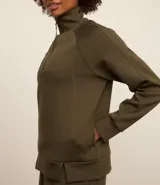 Buzo deportivo verde oliva de microfibra pesada, con cuello alto con cremallera, recorte en los hombros y dos aberturas en la parte de abajo.