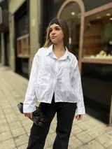 Camisa blanca de diseño oversize, con mangas largas, bolsillos frontales con solapa y cierre de botones.