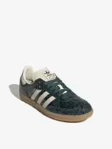 Zapatillas Adidas Samba OG con exterior de piel con estampado de piel de serpiente en tonos verde oscuro y negro. Cuentan con las 3 Franjas dentadas en color blanco crema, cordones verde oscuro, revestimientos en color crema claro y puntera en T reforzada. La suela es de caucho color caramelo.