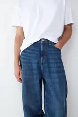 Jean de corte baggy y silueta holgada, confeccionado en denim de algodón color azul oscuro con efecto lavado. Presenta diseño clásico de cinco bolsillos, cintura con trabillas y cierre frontal con botón y cremallera.