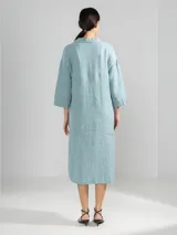 Camisa larga celeste confeccionada en lino, con cuello clásico, mangas 3/4, silueta fluida, dobladillo curvado en las costuras laterales y bolsillos discretos.