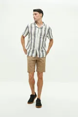 Camisa de manga corta con cuello cubano, confeccionada en una mezcla de lino y algodón con textura. Presenta un diseño a rayas verticales en tonos beige y celeste sobre fondo blanco, con cierre frontal de botones y logo bordado en el pecho.