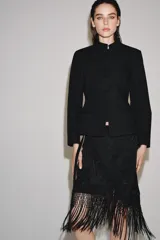 Falda corta de tiro medio, color negro, con diseño cruzado estilo pareo ajustable con lazada lateral. Cuenta con bordados tonales de motivos florales y bajo acabado con flecos largos.