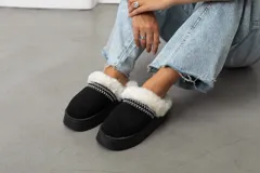 Pantuflas tipo slipper de gamuza negra con plataforma, forradas en su interior con piel sintética blanca y detalle de costura decorativa en el borde.