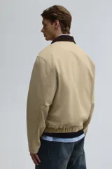 Campera tipo blouson de algodón color beige claro, con cuello de pana marrón oscuro. Posee cierre frontal, bolsillos delanteros ribeteados y elástico ajustable con cordón en el bajo.