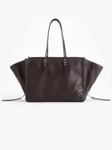 Cartera tote bag pequeña realizada en cuero vacuno marrón, con textura granulada, doble asa de hombro y bolsillos laterales con cierre. Presenta además un bolsillo frontal con cierre y detalle de tiracierres y llavero metálico colgante.